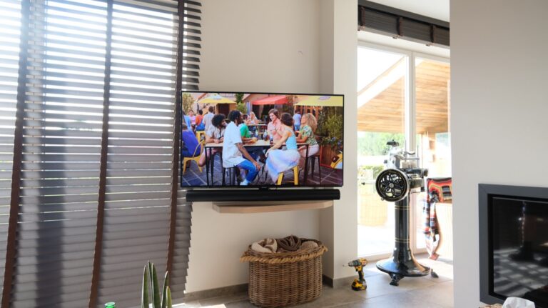 Tv op draaibare wandbeugel met SONOS soundbar naast de open haard in een privéwoning te Voorde