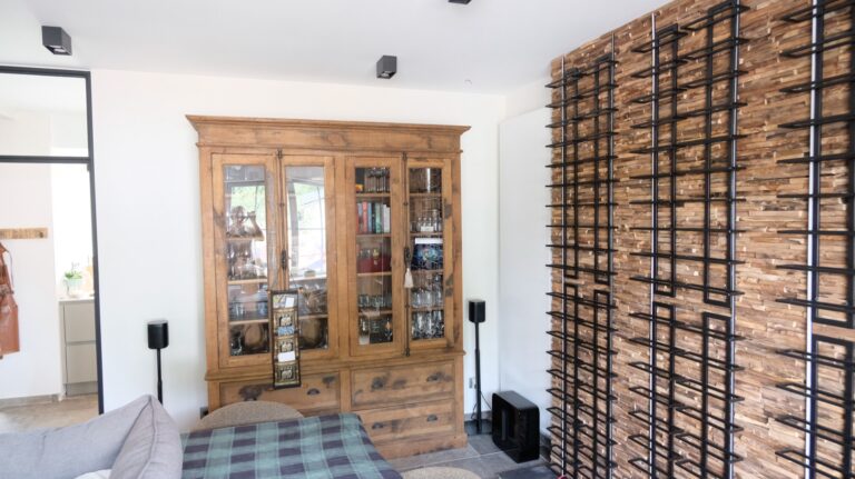 AUDAC-luidsprekers en subwoofer bij de vitrinekast en het wijnrek in een privéwoning te Voorde
